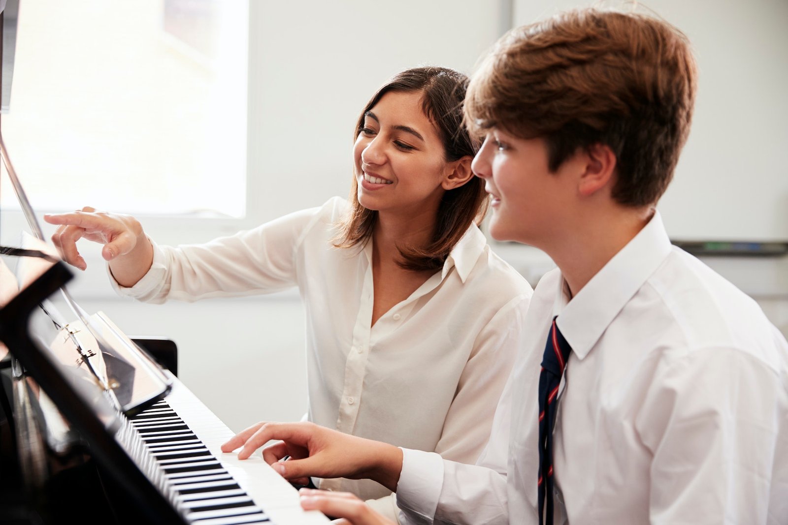 Male Pupil With Teacher Playing Piano In Music Lesson